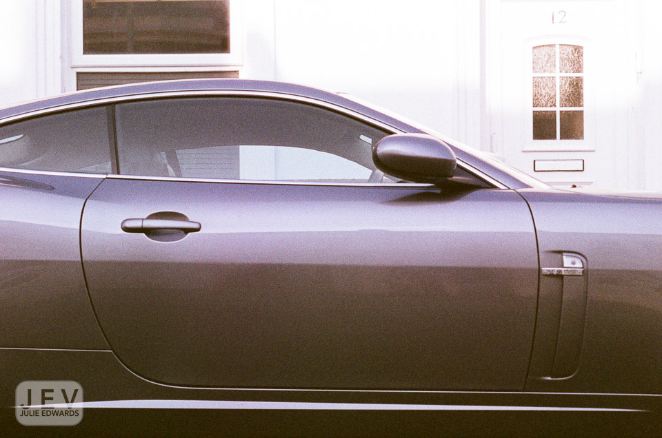 Side view of a sleek gray sports car parked near a white door.