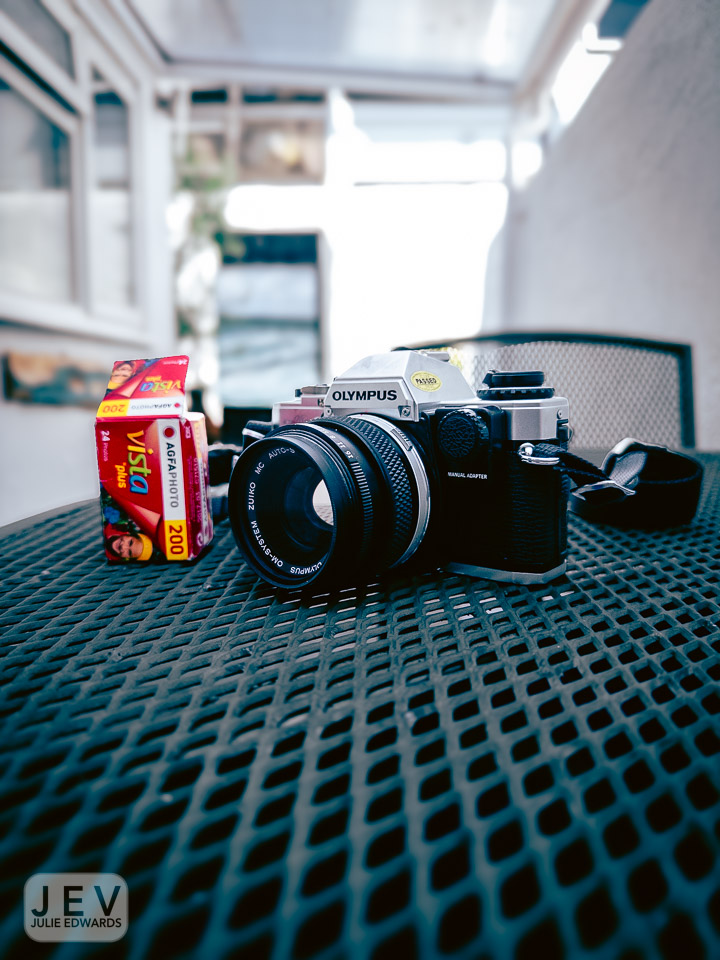 Olympus camera with a lens and a roll of AGFA Vista film on a table.
